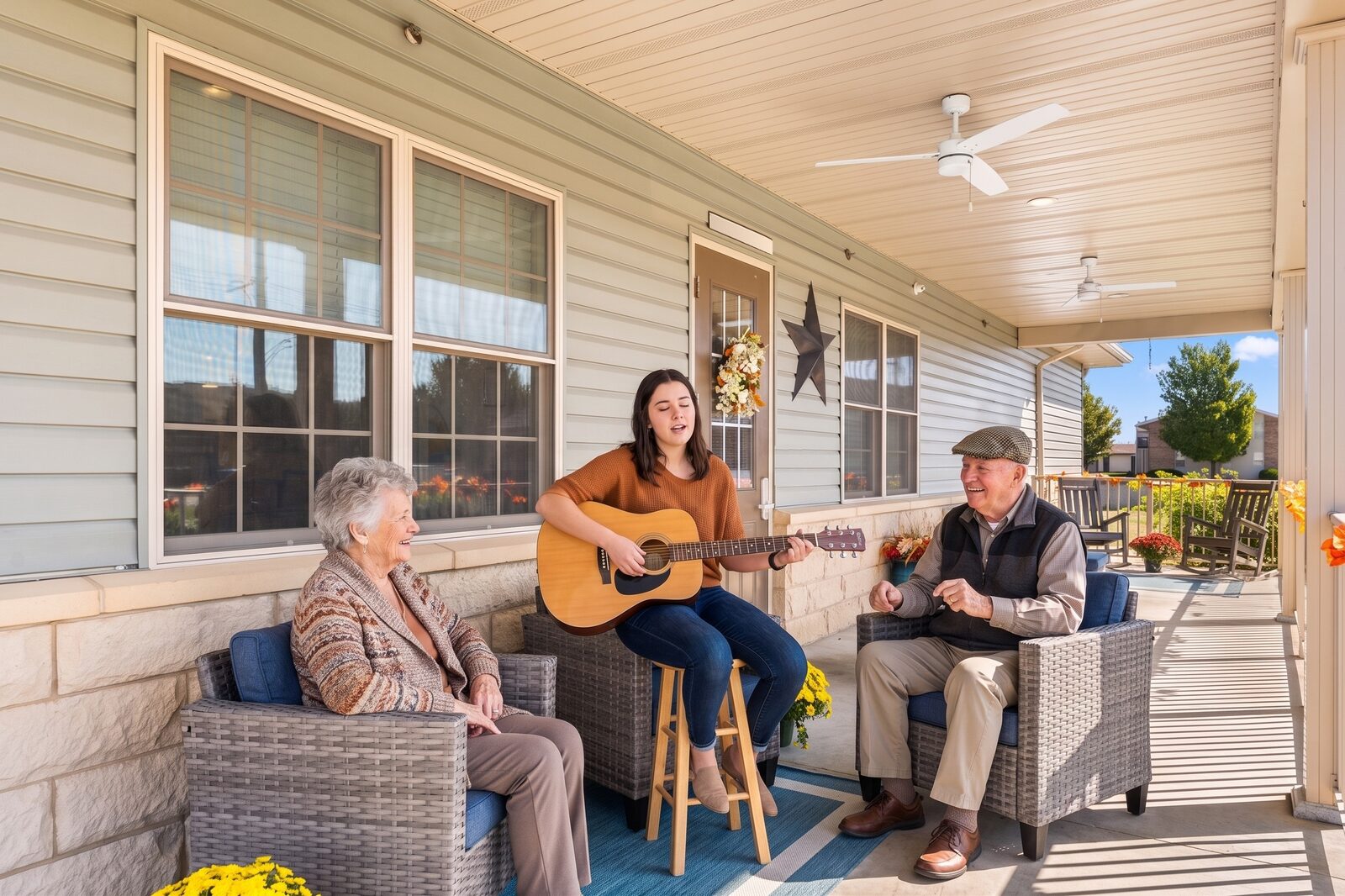 A young musician playing acoustic guitar for two smiling residents on the front porch at Savoy Place